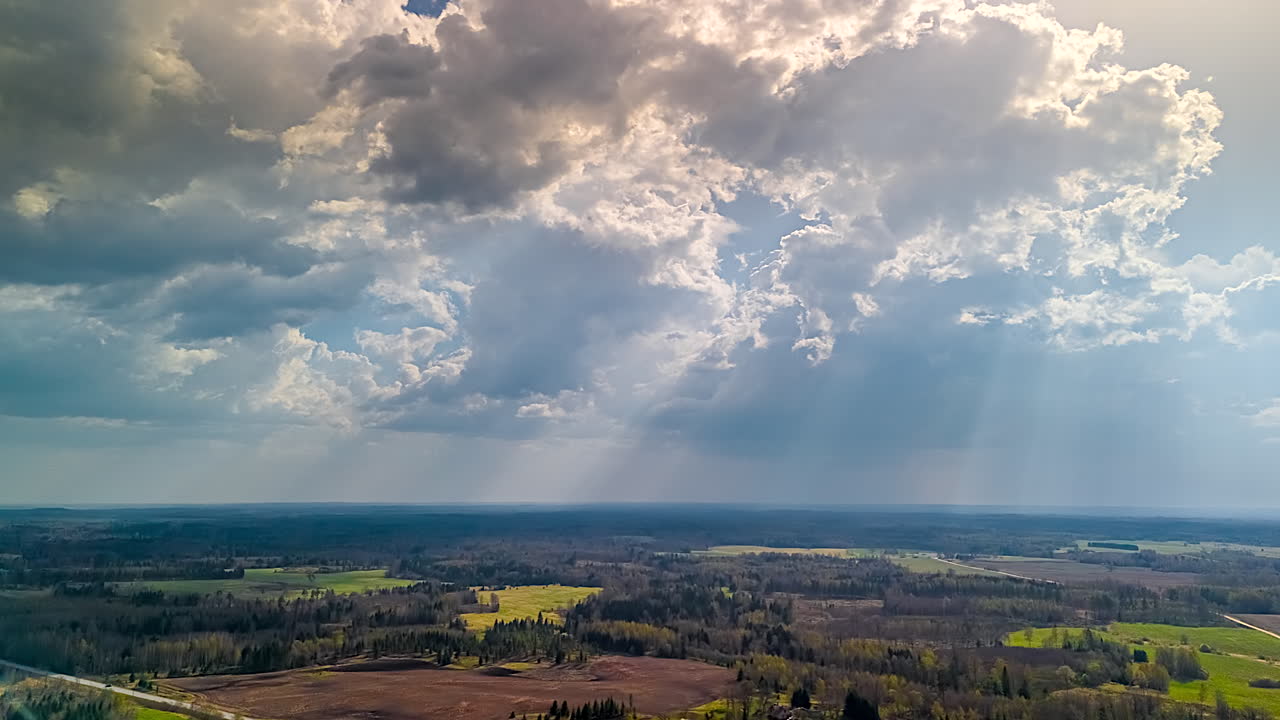 Sunrays shine through dark clouds drifting over a rural area.