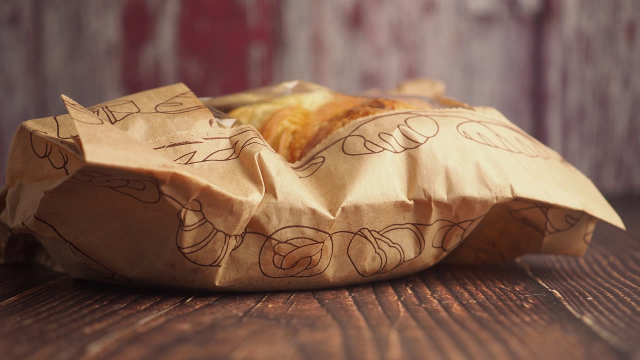 Golden Brown Pastry Wrapped in Paper Bag on Rustic Wooden Table