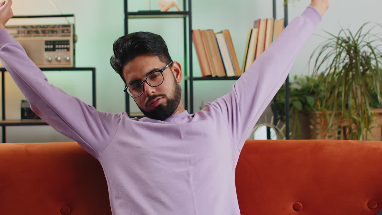 Tired indian man lying down on comfortable couch taking a rest daytime nap relaxing falling asleep