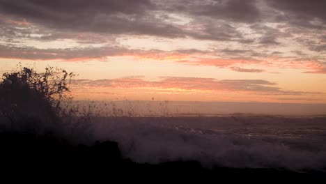 Rough-Atlantic-ocean-waves-crashing-against-rocky-shore-with-orange-sunset