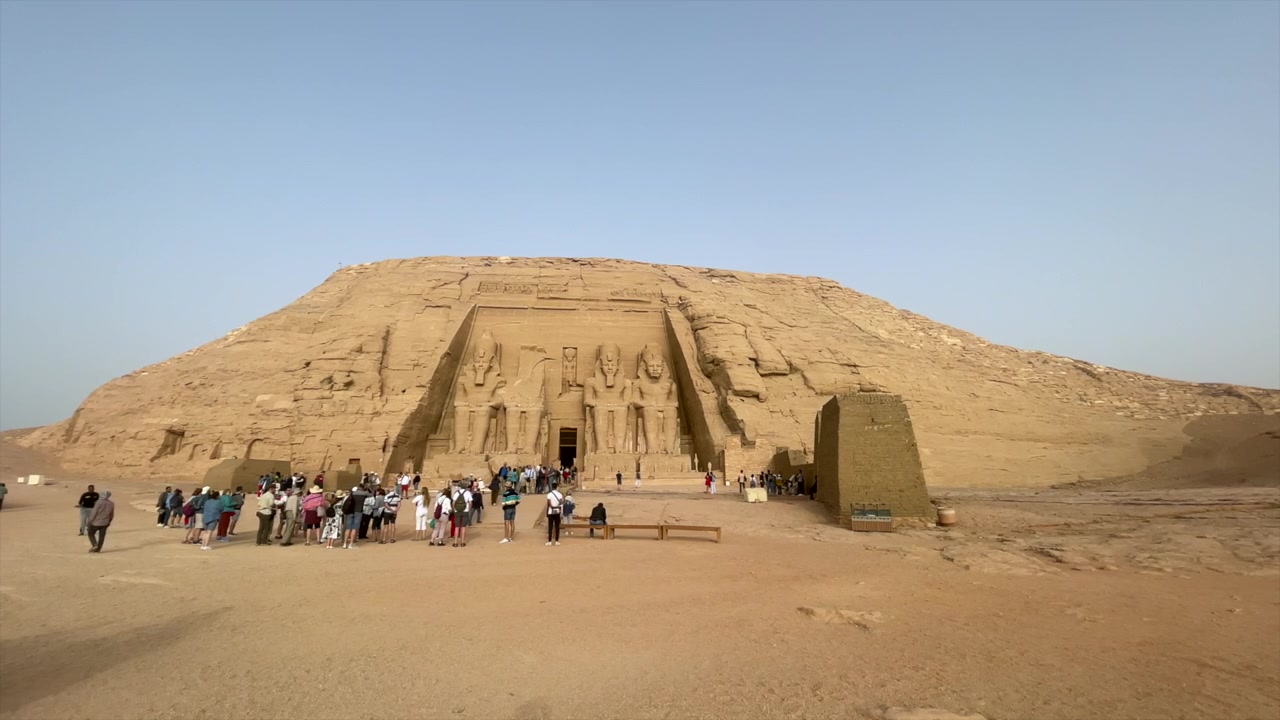 Ampia inquadratura panoramica del Tempio di Abu Simbel del Faraone Ramses II in Egitto. Turisti di fronte al monumento nubiano di Abu Simbel dell'antico Egitto, con cielo azzurro e un uccello che attraversa il cielo. Sito Patrimonio dell'Umanità UNESCO.