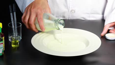 una persona con una bata de laboratorio vierte leche en un plato, rodeado de líquidos de colores, en un entorno controlado