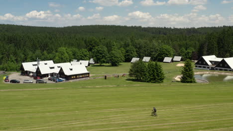 a lone person riding their bicycle down a sloping grass field above a luxury resort, aerial follow