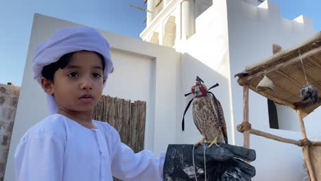 niño árabe en traje tradicional kandura con un pequeño halcón en la mano