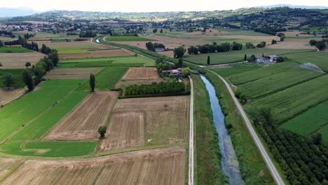 Toma-Aérea-De-Un-Amplio-Campo-En-Italia,-Siguiendo-Un-Río