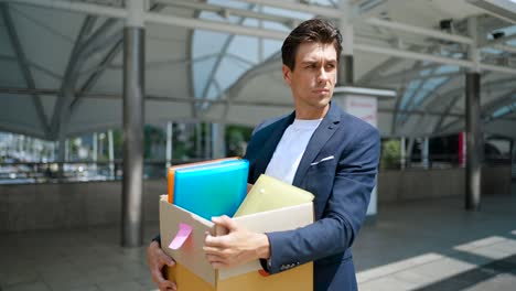 depressed businessman being fired by company downsizing carrying a box of personal items