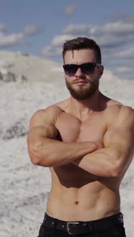 portrait of shirtless athlete. handsome guy with beard in sunglasses with muscular body posing on white canyon in summer. camera motion around. vertical video