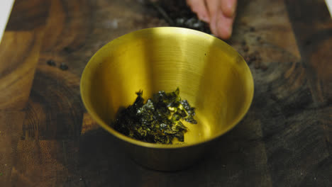 chef putting fresh seaweed inside golden bowl during cooking meal,slow motion