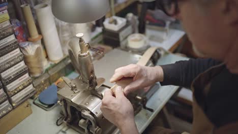 overhead view on hands of leather craftsman while thinning leather belt