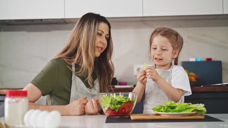 mujer mira a su hija rasgando lechuga fresca para cocinar ensalada