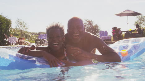 portrait of smiling senior couple on summer holiday relaxing in swimming pool on inflatable airbed