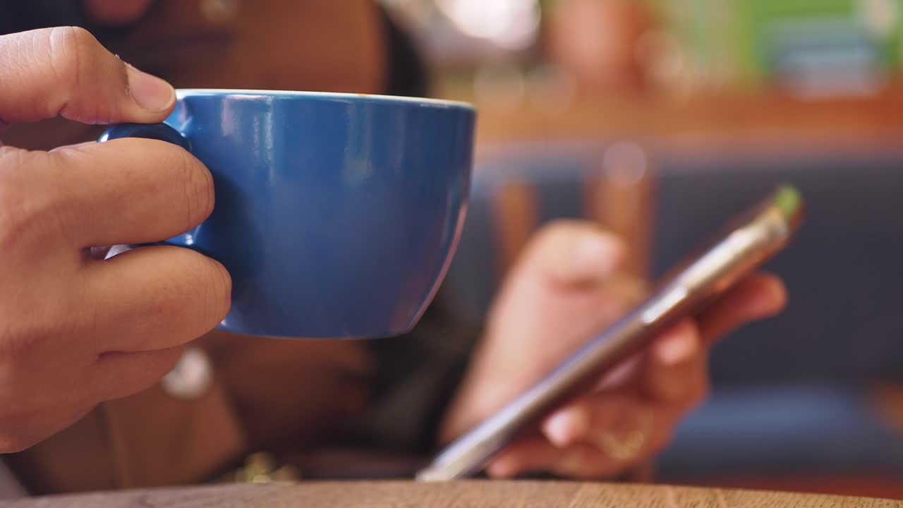 Person drinking coffee and using phone in a cafe