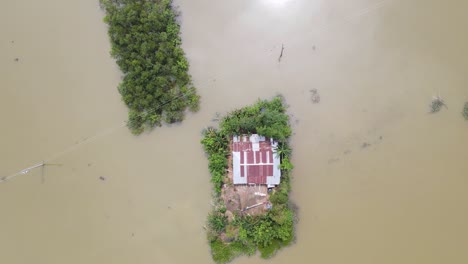 single tin-roof house isolated on a small patch of land in flood, aerial top down view