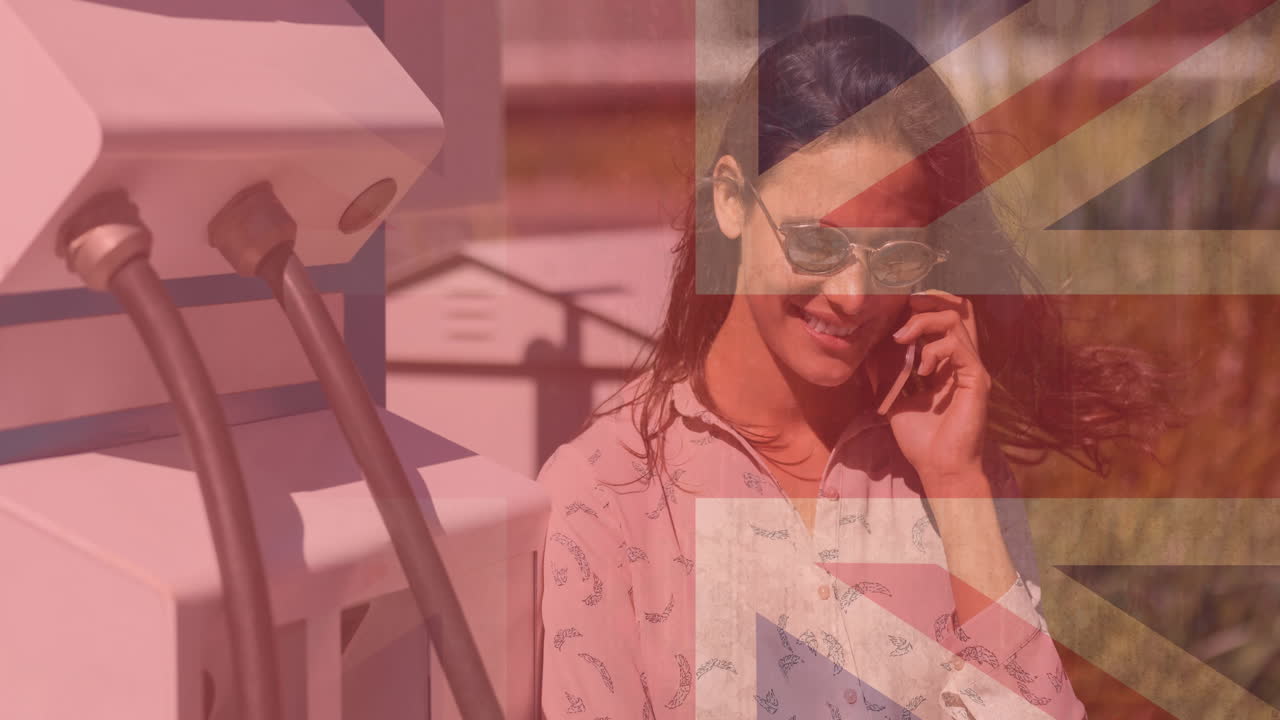 bandera de gran bretaña sobre una mujer caucásica sonriente usando un teléfono inteligente y cargando un coche eléctrico