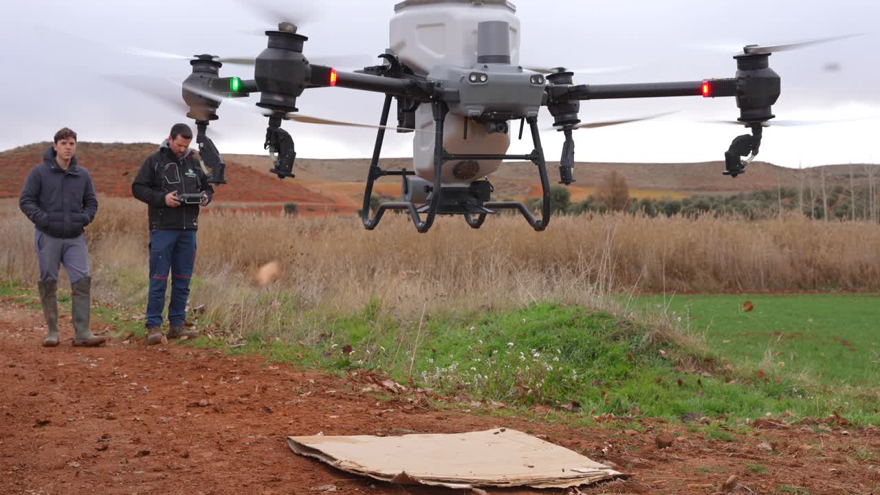 Agricoltori esperti di tecnologia lanciano un grande drone agricolo con un serbatoio per solidi da un campo coltivato per iniziare il trattamento delle colture.