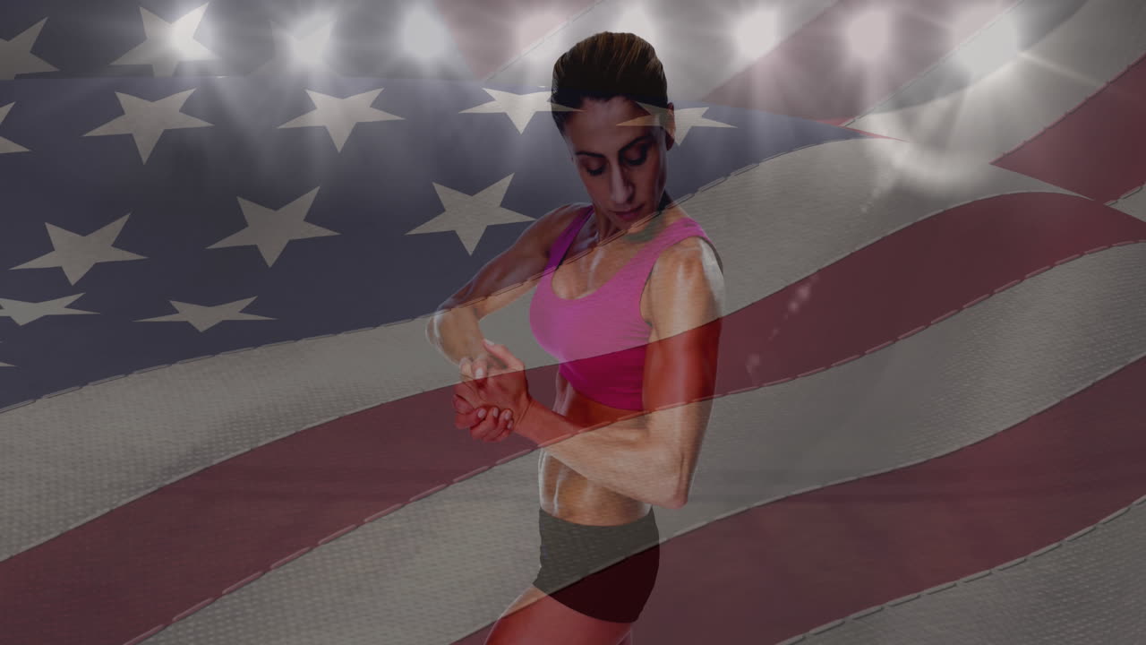 agitando la bandera estadounidense sobre una atleta flexionando sus bíceps contra un estadio deportivo en el fondo