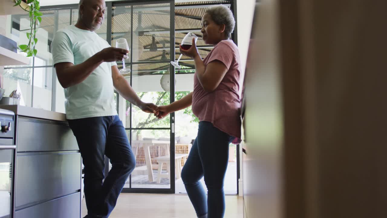 Happy african american senior couple drinking vine in kitchen