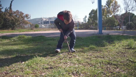 wide shot of toddler in the fields digging with a wooden stick 60fps