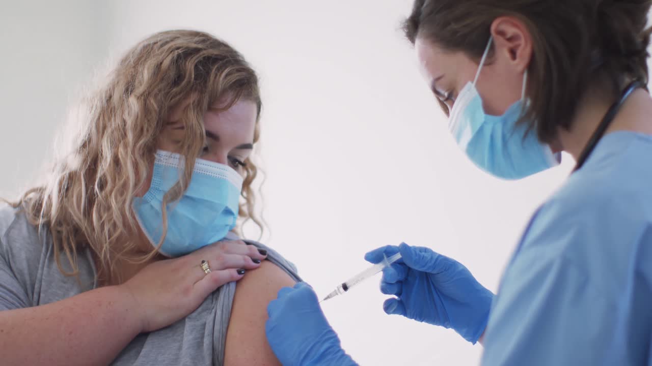 Dottoressa caucasica con mascherina che vaccina una donna caucasica a casa