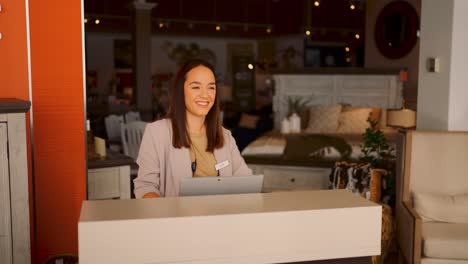 A-Young-Well-Dressed-Female-Furniture-Sales-Person-Walks-Out-From-Behind-a-Counter-to-the-Store-Entrance-and-Smiles-Taking-a-Deep-Breath