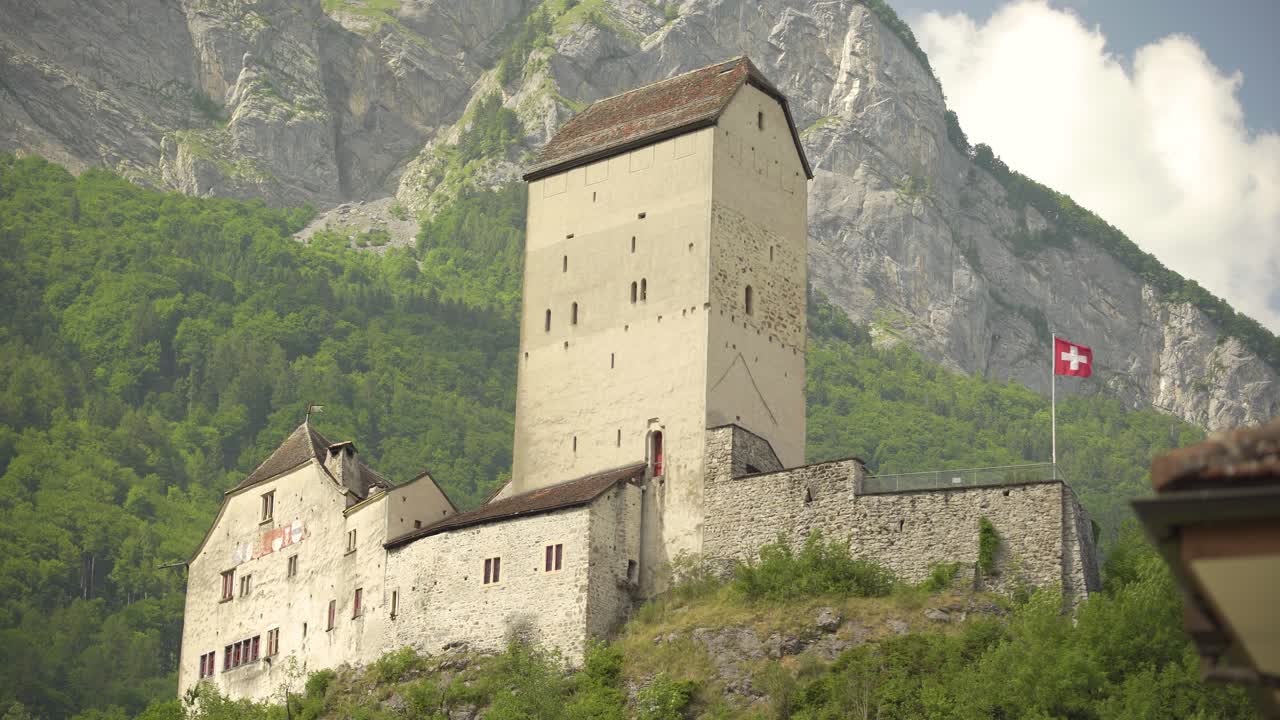 ángulo bajo del histórico castillo de sargans con bandera suiza ondeando en una colina cerca del monte gonzen rodeado por un denso bosque de pinos verdes, alpes suizos