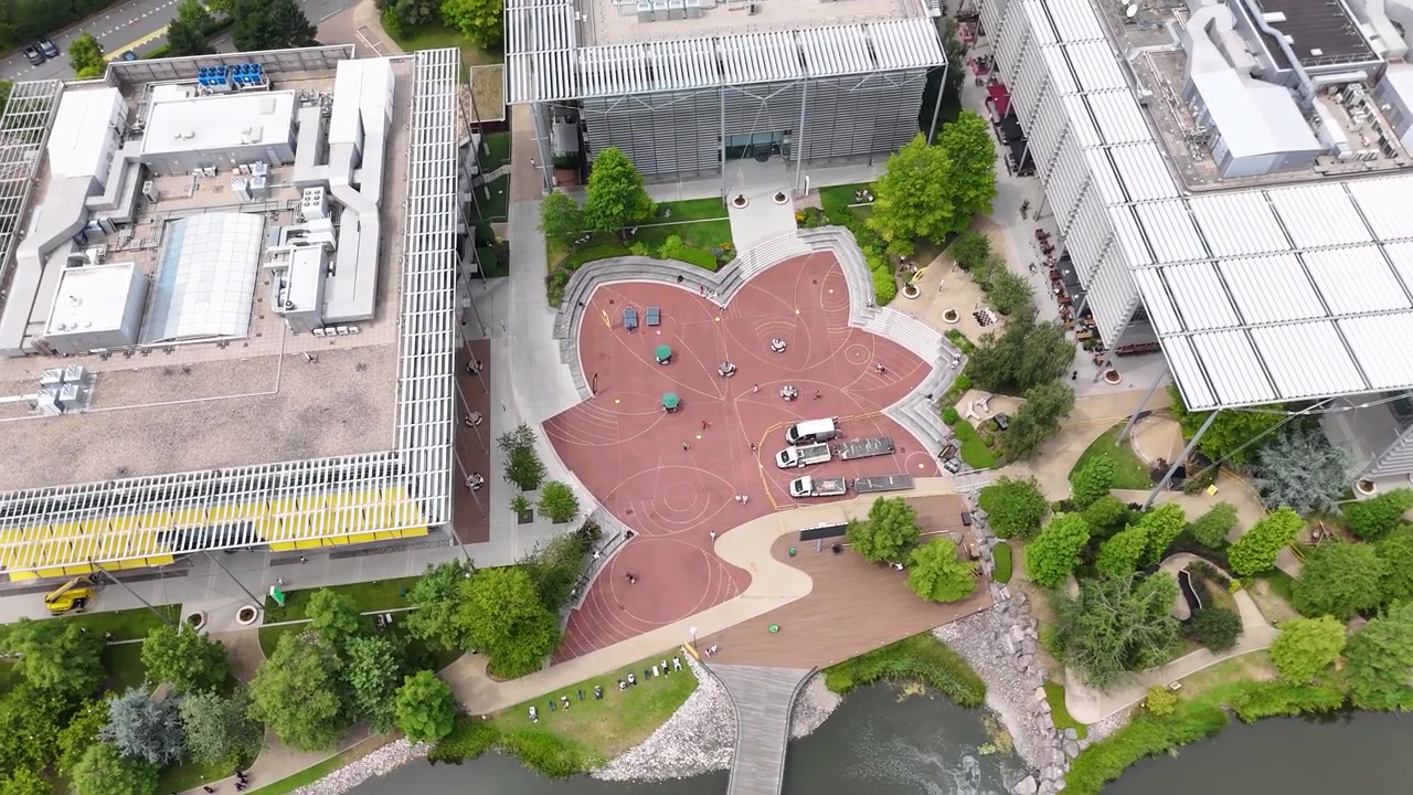 Plaza roja estampada y fuente de agua en el corazón de un moderno parque de oficinas, enmarcada por edificios acristalados y árboles
