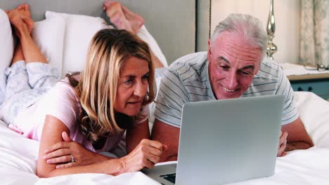 senior couple lying on bed and using laptop