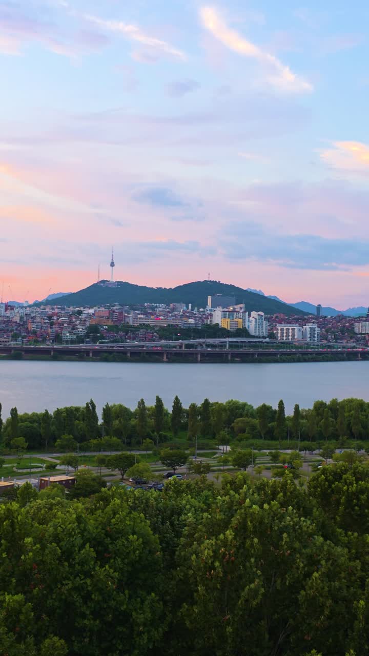A beautiful vertical aerial of colorful sunset sky over Namsan Tower, Han River, and lush green Hangang Park in Seoul, South Korea