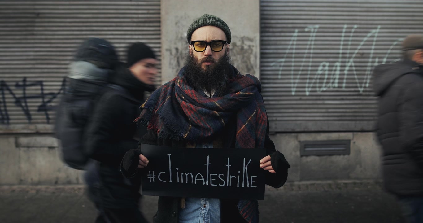 Giovane uomo che tiene un cartello per lo sciopero per il clima in una strada cittadina