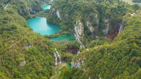 incredible aerial drone view of bright turquoise lakes connected with waterfalls between rocky cliffs and dense forest