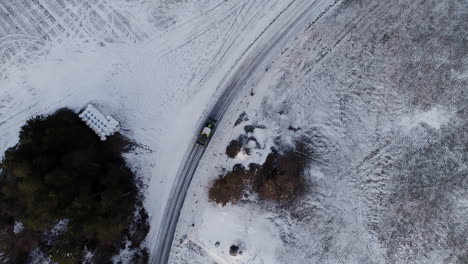 drone panning slowly above green claas tractor driving slowly on slippery icy road across fields filled with frosty snow in winter scandinavian nordic northern landscape cold frozen morning near lake