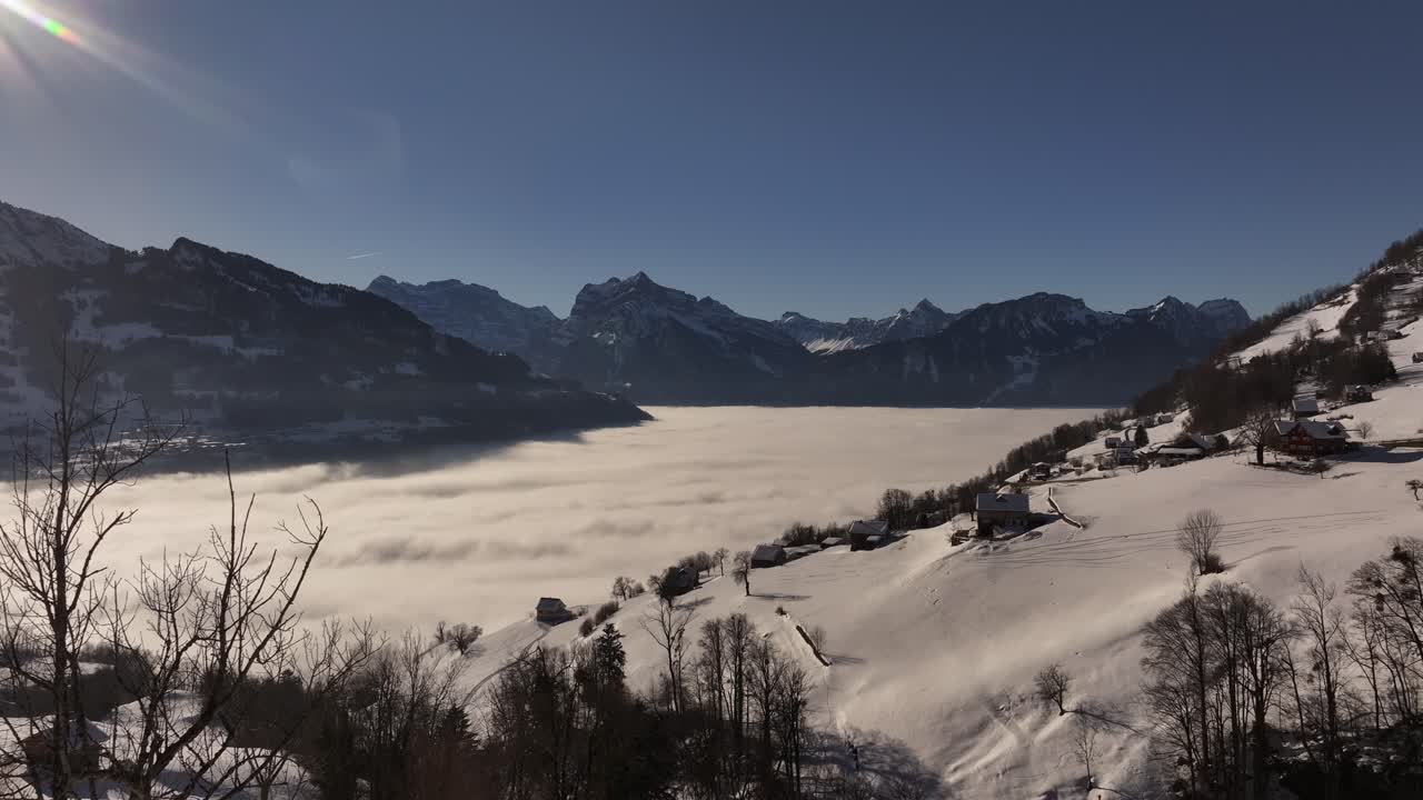 Drone pushes through thick clouds in Amden, Switzerland, snow-covered Swiss alps, serene valleys and breathtaking views of winter mountain landscape.