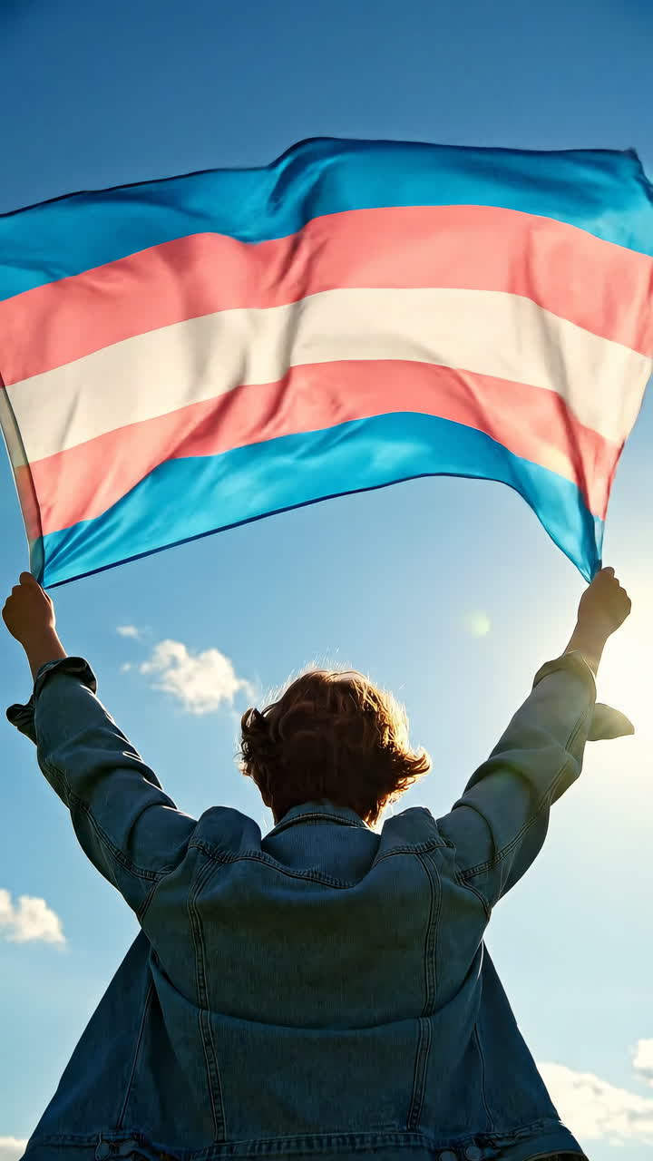 Persona che tiene in mano una bandiera transgender con cielo blu e luce solare sullo sfondo