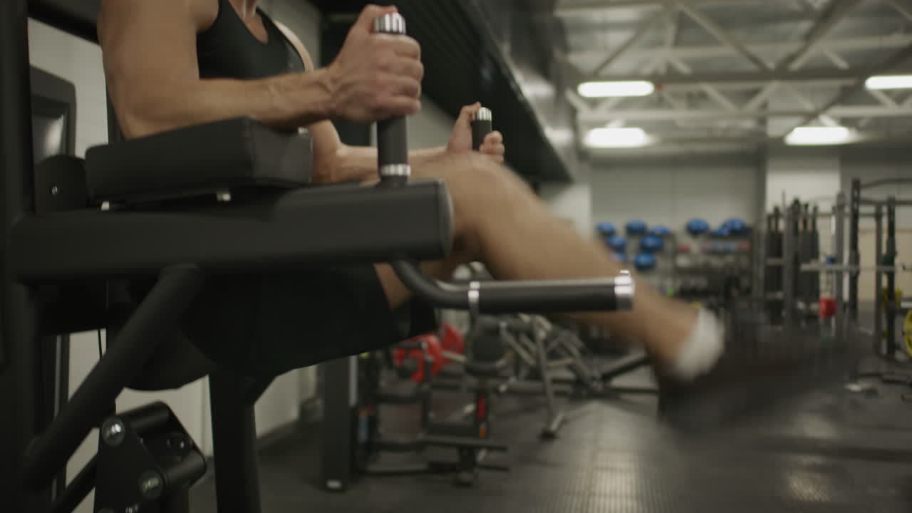 Hombre atlético realizando elevaciones de piernas colgantes durante entrenamiento de core en gimnasio