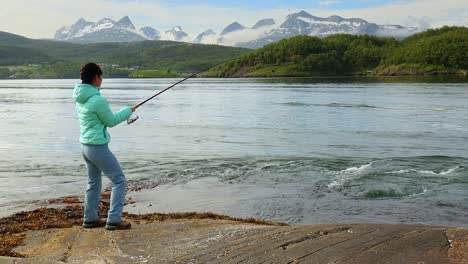una mujer atrapó un pez grande con una caña de pescar y no puede sacarlo del agua. pescar con una caña de pescar girando en noruega. pescar en noruega es una manera de abrazar el estilo de vida local.