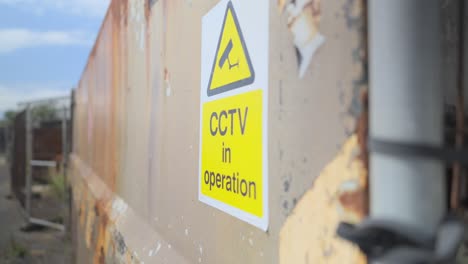 CCTV-in-operation-sign-close-up-in-derelict-urban-area,-slow-motion,-Fleetwood-Docks,-Lancashire,-UK