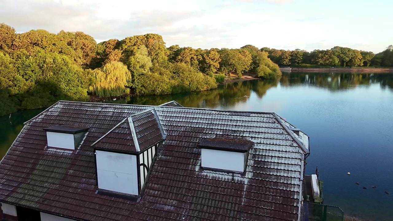 Luftaufnahme eines lebhaften Sonnenaufgangs über einem Waldsee mit einem verlassenen viktorianischen Bootshausdach