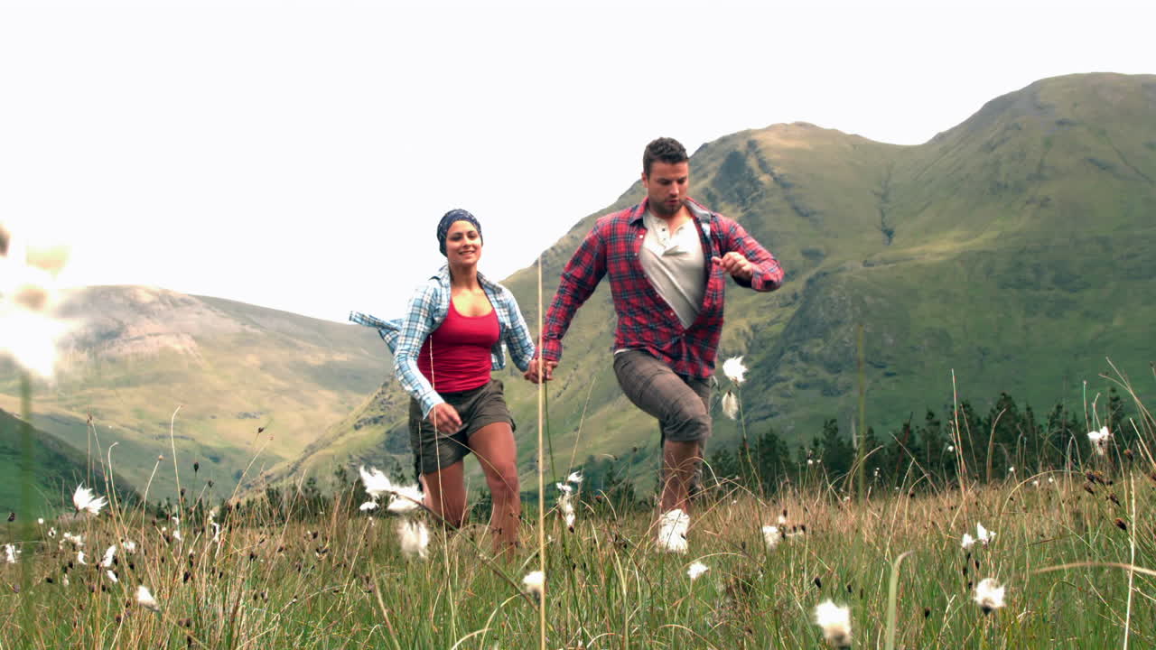 una pareja alegre corriendo de la mano por el campo.