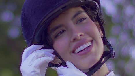 A-close-up-shot-captures-the-beautiful-smile-of-an-elegant-equestrian-woman-as-she-tightens-her-helmet-strap-in-preparation-for-her-ride
