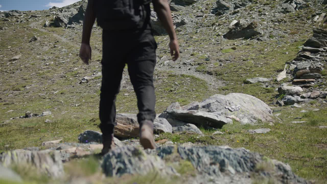Viaggiatore maschio di colore con zaino che attraversa lo schermo per esplorare il versante montuoso del Cervino in Svizzera.