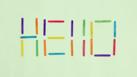 hello written with wooden colorful craft sticks move on pastel green background. stop motion flat lay