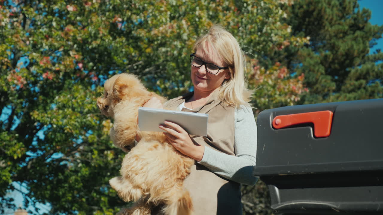 팔에 개를 안고 있는 여자가 우체통 근처의 서신을 살펴보고 있다