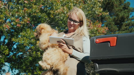 a woman with a dog in her arms looks through correspondence near the mailbox