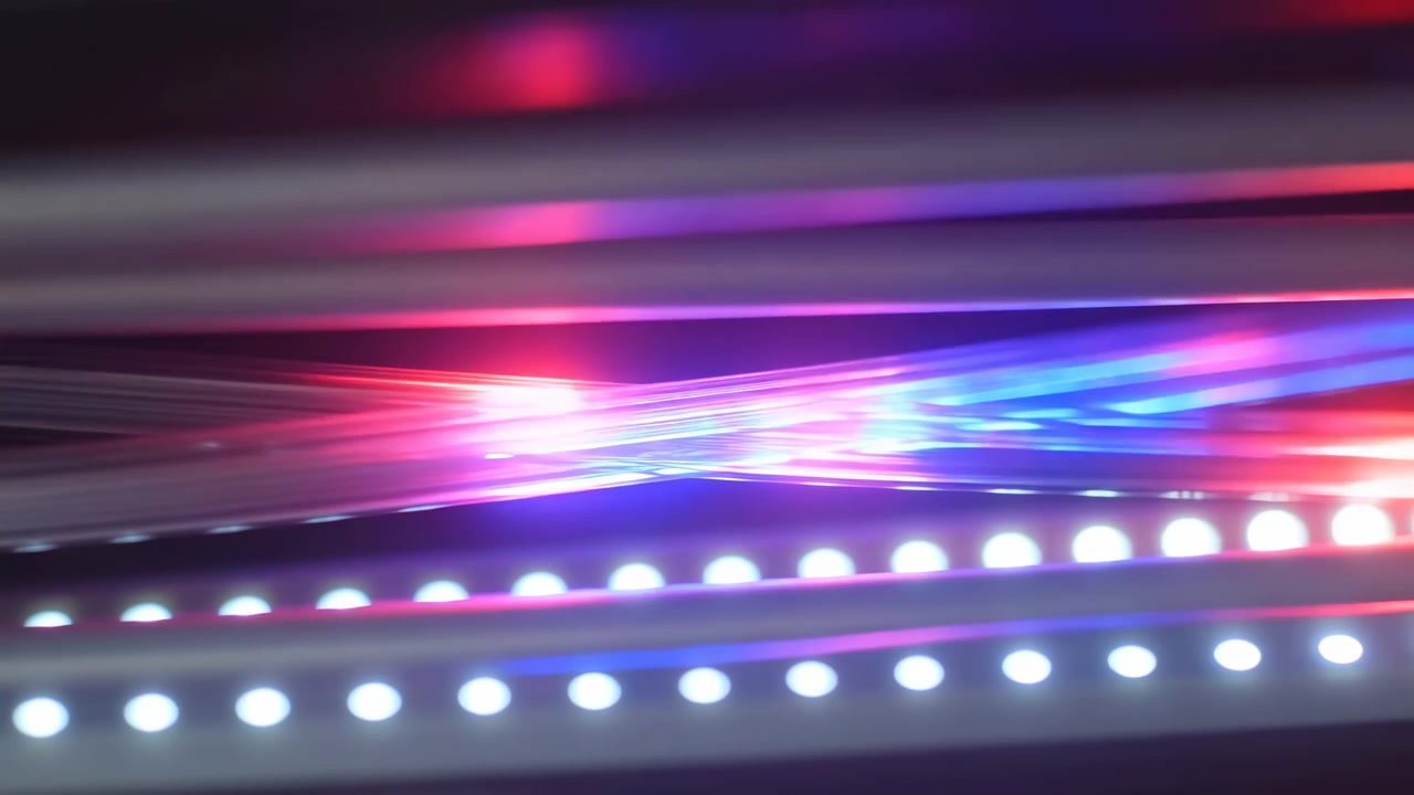 Blurred horizontal bands of red, blue, and white light sweep across a dark scene, with glowing dots along the bottom creating a fast, futuristic motion effect