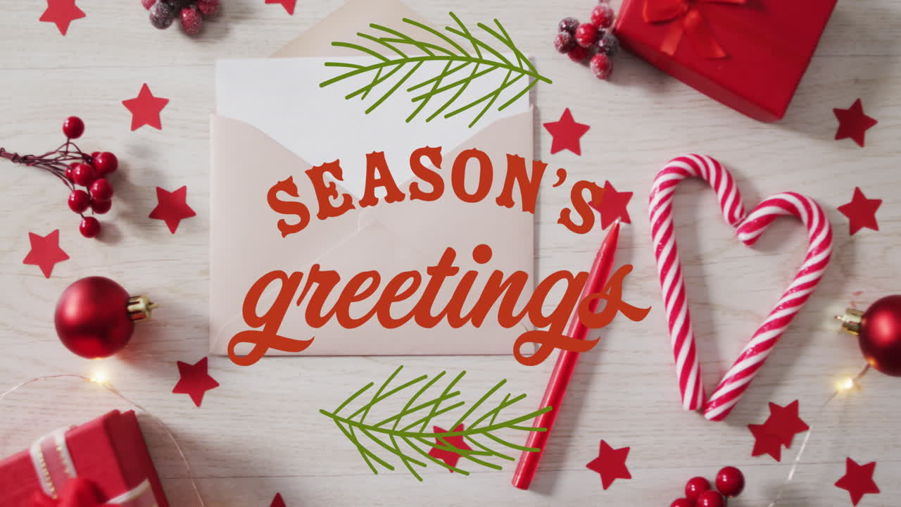 Animation of seasons greetings over envelope, stars, sticks, gift box, cherries and bauble on table