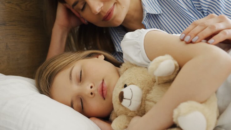 Close-up view of cute blonde little girl sleeping on the bed while hugging her teddy bear
