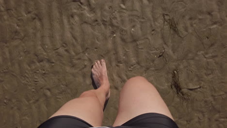punto di vista in prima persona pov di un uomo che cammina sulla sabbia bagnata, costume da bagno nero