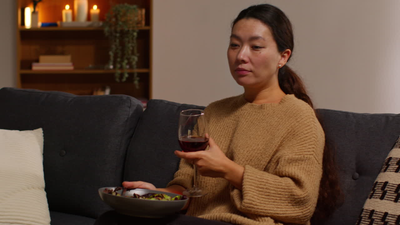 집에서 소파에 앉아 건강한 채식주의자 또는 채식주의자를 먹고 씨과 함께 러드 잎을 먹고 와인 한 잔을 입고 노트북 2에서 쇼를보고 있습니다.