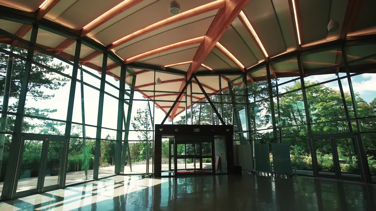 A slow push forward in a large, empty space surrounded by windows with a garden outside