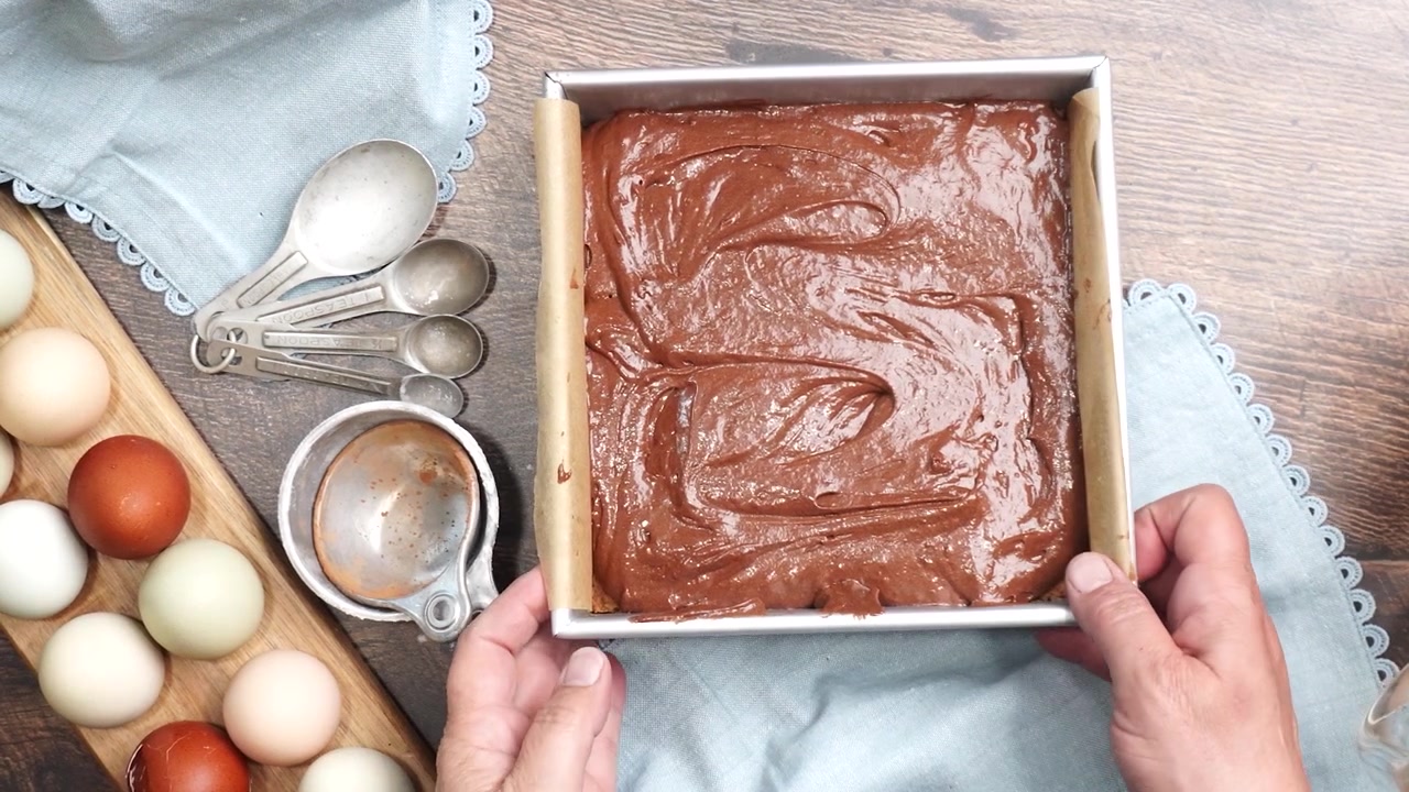 Baking delicious caramel pecan brownies. Picking up the baking pan to put the brownie batter in the oven. Freshly baked gooey chocolate brownies with sweet caramel and nutty pecans.